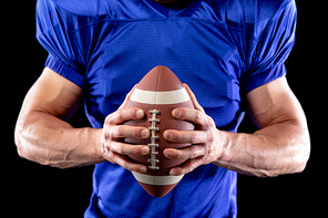 Front view mid section of a Caucasian male American football player wearing a team uniform and pads, holding a football in his hands