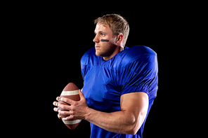 Side view of a Caucasian male American football player wearing a team uniform, pads and eye black under his eyes, holding a football in his hands