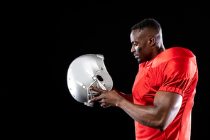 Side view of an African American male American football player wearing a team uniform and pads, holding his helmet before putting it on