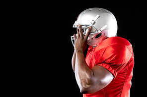 Side view of an African American male American football player wearing a team uniform and pads, putting on his helmet