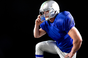 Side view of a Caucasian male American football player wearing a team uniform, pads and a helmet standing with one leg up and hand on hip, watching through the facemask of his helmet