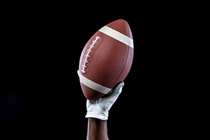 Close up of the raised hand of an African AMerican sportsman playing American football, wearing a glove and holding a football in the air