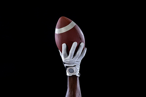 Close up of the raised hand of an African AMerican sportsman playing American football, wearing a glove and holding a football in the air