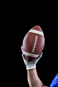 Close up of the raised hand of a Caucasian male American football player wearing a glove and holding a football in the air. Vertical shot