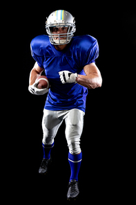 Front view of a Caucasian male American football player wearing a team uniform and a helmet, stepping forward holding a football under his arm. Vertical shot