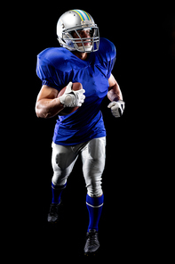 Front view of a Caucasian male American football player wearing a team uniform, pads and a helmet running with a football under his arm. Vertical shot