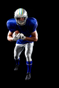 Portrait close up of a Caucasian male American football player wearing a team uniform, pads and a helmet, leaning forward holding a football to his chest