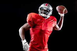 Front view of an African American male American football player wearing a team uniform, pads and a helmet perparing to throw a football