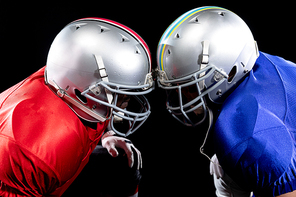 Side view of two American football players wearing team colours, pads and helmets kneeling opposite each other, their helmets touching