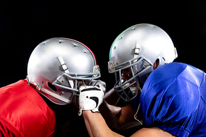 Side view of two American football players wearing team colours, pads and helmets standing opposite pulling at each others helmets