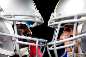 Side view close up of a Caucasian and an African American male American football player wearing helmets standing opposite staring at each other, their helmets touching