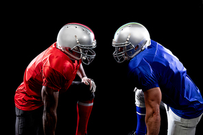 Side view of a Caucasian and an African American male American football player wearing helmets and their opposing team colours, standing opposite staring at each other