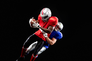 Front view of an African American male American football player wearing team colours and helmet being tackled from behind by a Caucasian male player from the opposing team