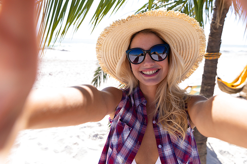 Caucasian woman enjoying time at the beach, standing by a palm tree, taking a selfie