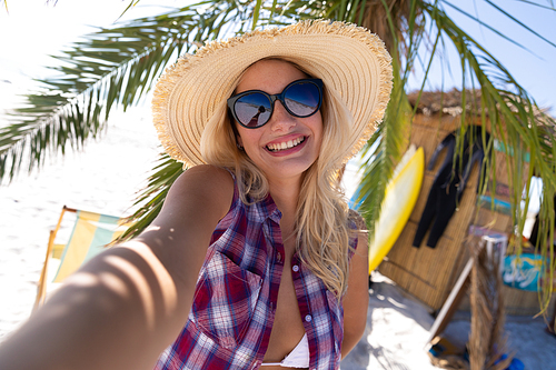 Caucasian woman enjoying time at the beach, standing by a palm tree, taking a selfie