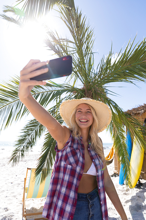 Caucasian woman enjoying time at the beach, standing by a palm tree, taking a selfie