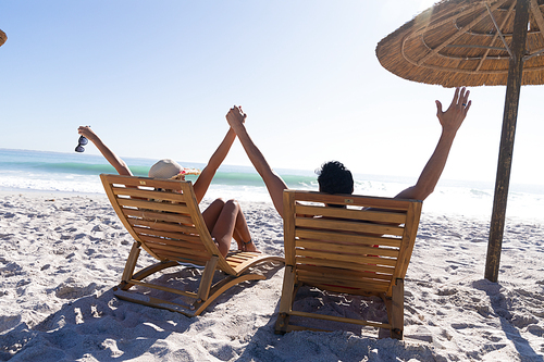 Caucasian couple enjoying time at the beach on a sunny day, sitting on deck chairs and holding hands with sea in the background