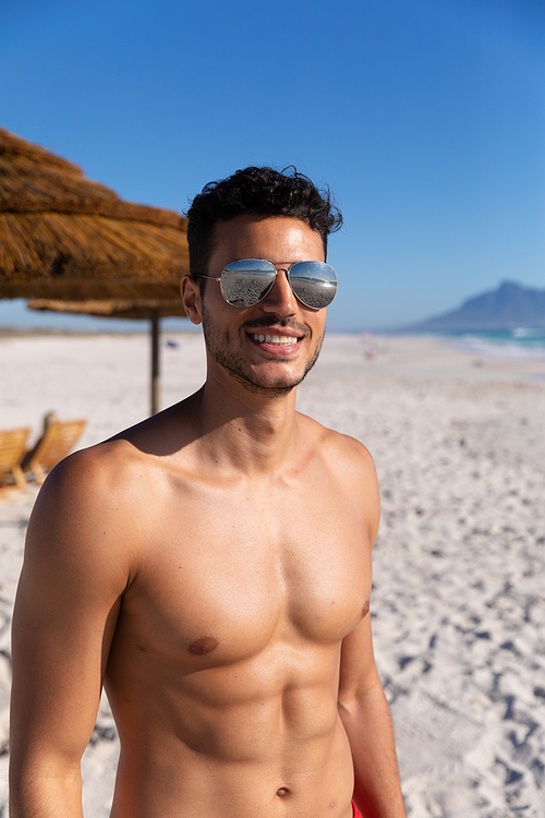 Caucasian man enjoying time at the beach on a sunny day, standing and looking at the camera with blue sky in the background