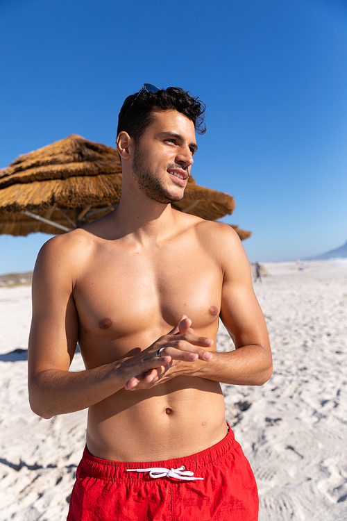 Caucasian man enjoying time at the beach on a sunny day, standing and looking away with blue sky in the background