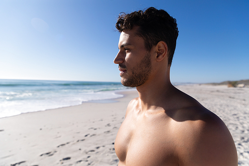 Caucasian man enjoying time at the beach on a sunny day, standing and looking away with sea in the background