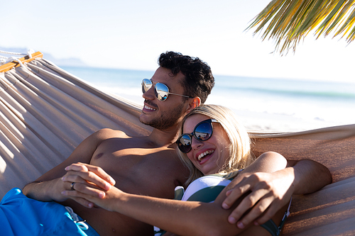 Caucasian couple enjoying time at the beach, lying on a hammock, embracing and holding hands