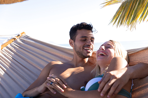 Caucasian couple enjoying time at the beach, lying on a hammock, embracing and holding hands