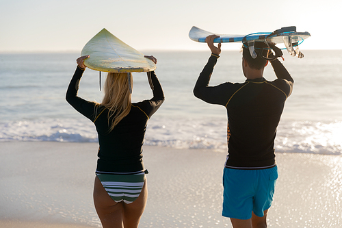 Caucasian couple enjoying time at the beach, holding surfboards above their heads, walking towards the sea
