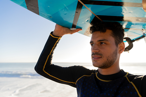 Caucasian man enjoying time at the beach on a sunny day, holding a surfboard above his head with sea in the background