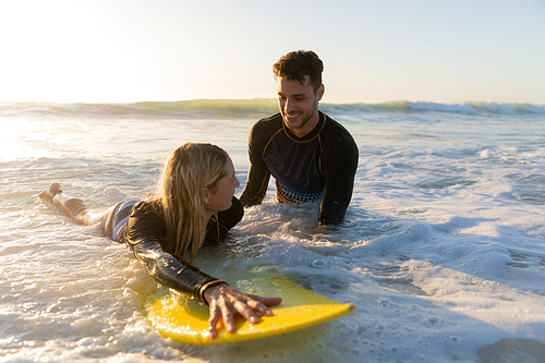 Caucasian couple enjoying time at the beach on a sunny day, a woman is lying on a surfboard with sea in the background