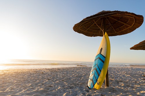 Magnificent view of two surfboards leaning on an umbrella on a beach on a sunny day with blue sea and sky in the background