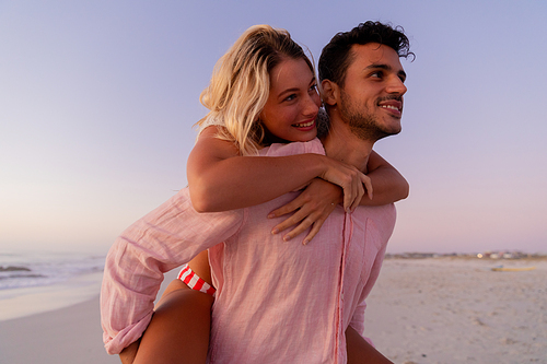 Caucasian couple enjoying time at the beach, a man is holding a woman piggy back