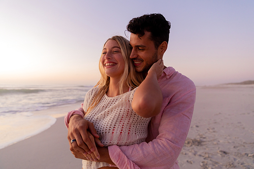 Caucasian couple enjoying time at the beach during a pretty sunset, embracing with yellow sand, blue sea and sky in the background