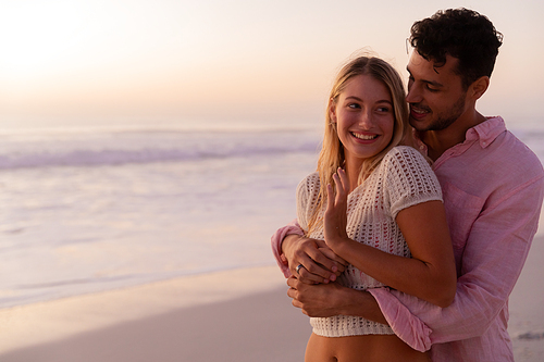 Caucasian couple enjoying time at the beach during a pretty sunset, embracing with yellow sand, blue sea and sky in the background