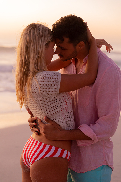 Caucasian couple enjoying time at the beach during a pretty sunset, embracing and kissing with blue sky and sea in the background