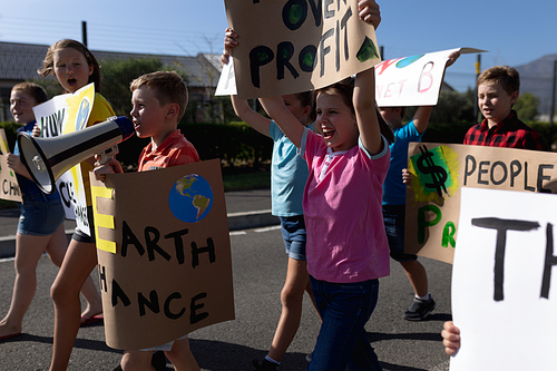 Side view of a group of Caucasian elementary school pupils on a protest march, carrying signs with environmental and conservation slogans on them, and one boy shouting in a megaphone