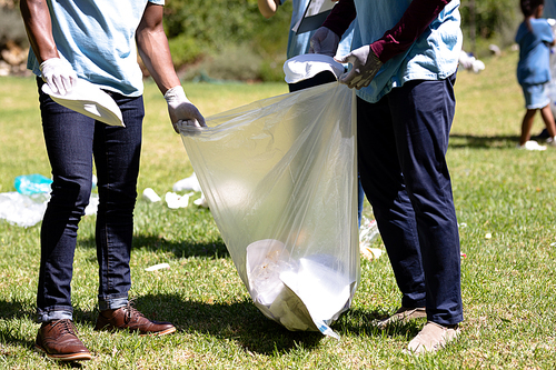 Mid section view of a multi-generation mixed race family spending time outside together, all wearing blue volunteer t shirts and protective gloves, collecting garbage, holding a garbage bag, on a sunny day