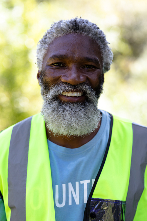 Portrait of a senior African American man standing in a garden, wearing blue volunteer t shirt, looking at the camera and smiling, on a sunny day