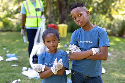 Portrait of a mixed race boy and girl spending time outside with their family, crossing their hands, looking at the camera, with their family in the background, all wearing blue volunteers t shirts, on a sunny day
