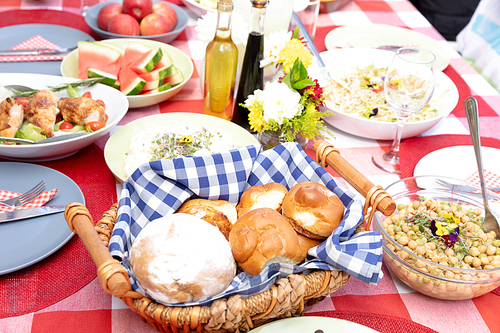 Close up view of a table set with fresh salads, fruits and basket with bread and rolls during a family lunch in the garden on a sunny day.