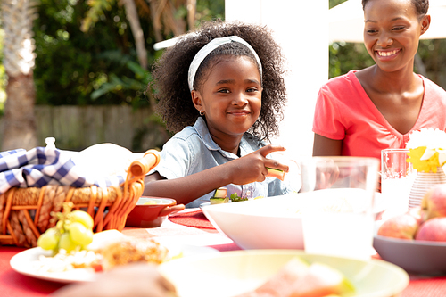 African American girl smiling and looking into a camera during a family lunch in the garden on a sunny day.