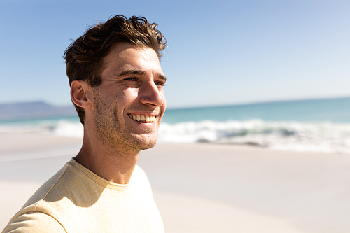 Caucasian man enjoying his time at the beach with his friends on a sunny day, looking away and smiling