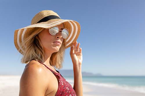 Caucasian woman enjoying her time at the beach with her friends on a sunny day, wearing sunglasses and hat and looking away