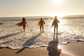 Two mixed race and a Caucasian men enjoying their time at the beach with their friends on a sunny day, running from the sea, holding surfboards