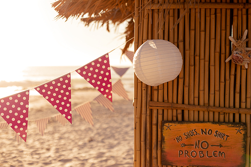 Garlands and a white lantern are hanging from a surfing lessons hut with a sea in the background on a  sunny day
