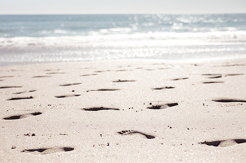 Footprints in the sand on a sunny, sandy beach, with calm sea on the horizon and blue sky in the background