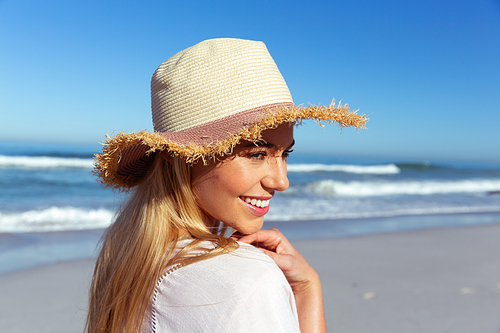 Close up of a Caucasian woman enjoying time at the beach on a sunny day, wearing a hat, smiling, with sea in the background