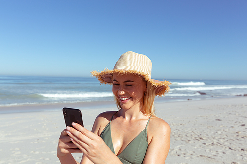 A Caucasian woman enjoying time at the beach on a sunny day, using her smartphone, with sea in the background