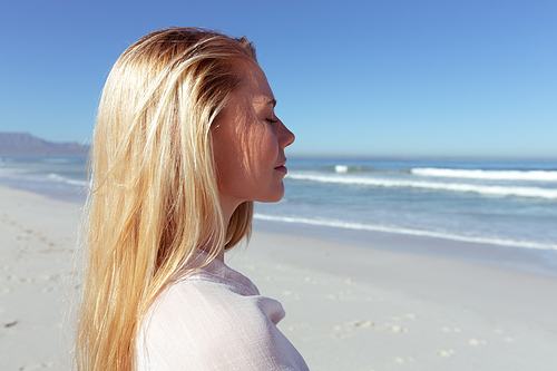 Close up of a Caucasian woman enjoying time at the beach on a sunny day, standing with her eyes closed, with sea in the background