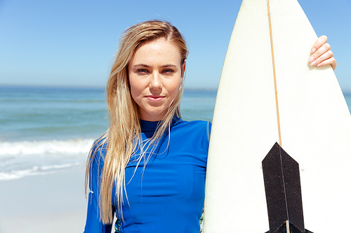 Portrait of a Caucasian woman enjoying time at the beach on a sunny day, holding a surfboard,  and smiling, with sea in the background