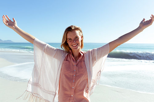Portrait of a Caucasian woman enjoying time at the beach on a sunny day, widening her arms and smiling, , with sea in the background